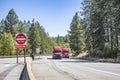 Two red big rig semi trucks with semi trailers transporting cargo running side by side on the turning wide highway road with exit Royalty Free Stock Photo