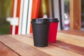 Two red and black paper cups to takeaway on wooden floor outside the cafe. Surfing boards stand behind at the background. Royalty Free Stock Photo