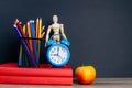 Two red books stand on the table, on the books there are blue watches and a glass with multi-colored pencils, behind the clock Royalty Free Stock Photo