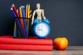 Two red books stand on the table, on the books there are blue watches and a glass with multi-colored pencils, behind the clock Royalty Free Stock Photo