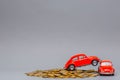 Two red car figurines placed on top of a heap of golden coins, on gray background