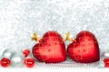 Two red Christmas tree glass balls in the shape of heart with golden stars and silver and red balls on shiny sparkling tinsel Royalty Free Stock Photo