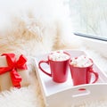 Two red cup of hot chocolate with marshmallow on white windowsill with furskin for rest. Holiday. Royalty Free Stock Photo