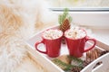 Two red cup of hot chocolate with marshmallow on white windowsill with furskin for rest. Holiday. Christmas morning.