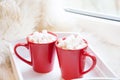 Two red cup of hot chocolate with marshmallow on white windowsill with furskin for rest. Holiday concept. Home.