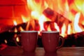 Two red cups in close-up against a burning fire fireplace Royalty Free Stock Photo