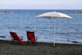 Two Red Deck Chairs and a Sun Umbrella on a Dark Sanded Beach in Cyprus Royalty Free Stock Photo