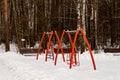 Two red double children swing on the playground on winter day in park background Royalty Free Stock Photo