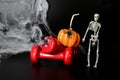 Two red dumbbells, skeleton, pumpkin, spider web on black background with copy space. Concept of Halloween, benefits of sports