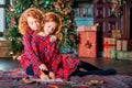 Two red-haired curly-haired girls write letter to Santa against the backdrop of Christmas tree and a decorated room