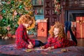 Two red-haired curly-haired girls write letter to Santa against the backdrop of Christmas tree and a decorated room