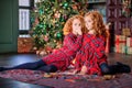 Two red-haired curly-haired girls write letter to Santa against the backdrop of Christmas tree and a decorated room