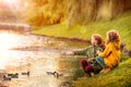 Two red-haired schoolgirl girls, sisters, cheerfully feeding ducks on the bank of a pond in a city park during the golden autumn Royalty Free Stock Photo