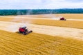 Two red harvesters harvests wheat on the field.