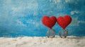 Two red heart-shaped decorations on sandy surface against blue backdrop Royalty Free Stock Photo