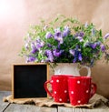 Two red mugs with a pattern of polka dots on an old wooden table, against the background of a jug with a bouquet of wildflowers. Royalty Free Stock Photo