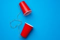 Two red paper cups connected with rope on blue background, toy telephone Royalty Free Stock Photo