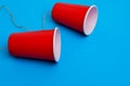 Two red paper cups connected with rope on blue background, toy telephone Royalty Free Stock Photo