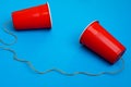 Two red paper cups connected with rope on blue background, toy telephone Royalty Free Stock Photo