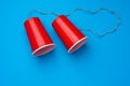 Two red paper cups connected with rope on blue background, toy telephone Royalty Free Stock Photo