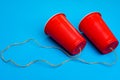 Two red paper cups connected with rope on blue background, toy telephone Royalty Free Stock Photo