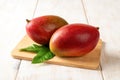 Two red ripe Palmer mangoes on a cutting board over white wooden table. Ready to eat whole sweet tasty mango. Two delicious