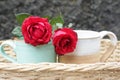 Two red roses and couple cup of tea or coffee in a wooden rattan basket on blue background. Relationship and valentine day concept Royalty Free Stock Photo