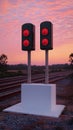 Two red traffic lights are mounted on a white platform with wooden posts against a sunset sky Royalty Free Stock Photo