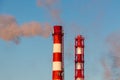 Two red and white chimneys of a boiler with orange smoke against a blue sky in sunny day Royalty Free Stock Photo