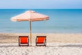 Two red wooden chairs and beach umbrella setting on white sand with seascape and blue sky in the background. Royalty Free Stock Photo