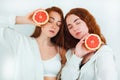 Two redheaded young women both look attractive standing on isolated white backgroung with grapefruits in their hands, beauty