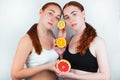 Two redheaded young women holding half of grapefruit and two halves of oranges in hands standing on isolated white background,