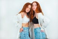 Two redheaded young women looking stylish wearing casual denim with shirt standing close to each other on isolated white