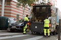 Two refuse collection workers loading garbage into waste truck emptying containers