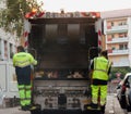 Two refuse collection workers loading garbage into waste truck emptying containers