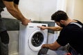 Two repairmen, workers in uniform working, reading washing symboles on washing mashine before fixing it, holding