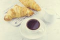 Two ÃÂ°resh croissants on a wooden vintage board in provence style with a cup of hot black coffee out of focus