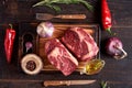 Two rib eye steaks on a cutting board with peppercorns, rosemary, olive oil, red chili peppers, onions and garlic Royalty Free Stock Photo