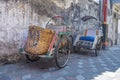 two rickshaws parked on the sidewalk with a plain and dull wall in the background Royalty Free Stock Photo