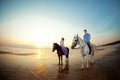 Two riders on horseback at sunset on the beach. Lovers ride horseback. Young beautiful man and woman with a horse at the sea. Rom Royalty Free Stock Photo