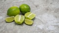 Two ripe limes, two lime sections and lime wedges on a marble kitchen counter