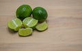 Two ripe limes, two lime sections and lime wedges on a wooden kitchen table