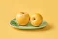 Two ripe yellow apples on a green plate over yellow background. Juicy organic fruits for antioxidant healthy eating. Vitamin