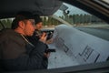 Two robbers sitting inside a car with guns looking at the blueprint of the building