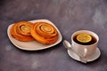 Two rolled buns with sugar and cinnamon on a white plate and a cup of black tea with a slice of lemon on a gray background