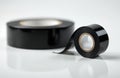 Two rolls of black electrical tape sit on a reflective white surface. One roll is in sharp focus, showing its vinyl material and Royalty Free Stock Photo
