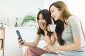 Two roommates using their smart phones sitting on a sofa at home