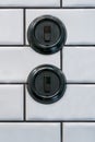 Two round black decorative bakelite light switches on white tile bathroom wall. Royalty Free Stock Photo