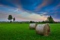 Two round hay bales lying on a green meadow, horizon and colorful clouds Royalty Free Stock Photo