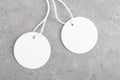 Two round white tag mockup with white cord, close up. Blank paper price tag isolated on grey stone background